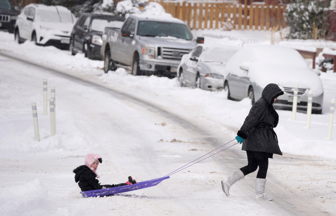 A woman pulls a child on a sled across the intersection of Bayaud Avenue and South Washington Street as a winter storm sweeps over the intermountain West