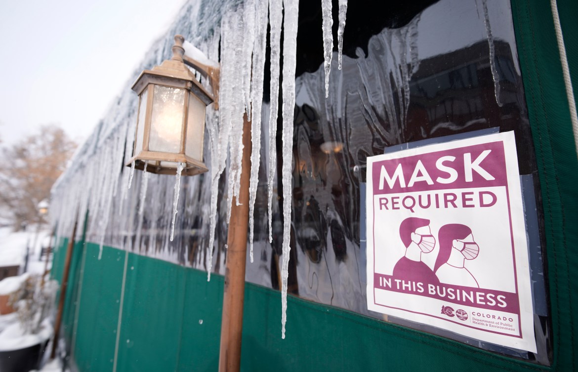 A sign advises patrons of COVID-19 restriction while long icicles grow from an awning outside a restaurant as a winter storm sweeps over the intermountain West Wednesday Feb. 2, 2022, in Denver.