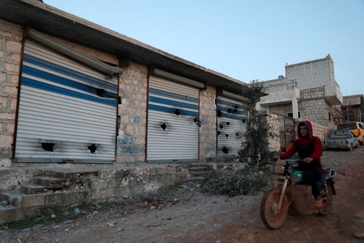 A Syrian man rides his motorcycle along damaged shops