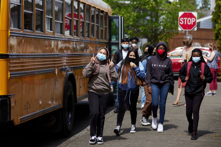 Children wearing masks beside school bus