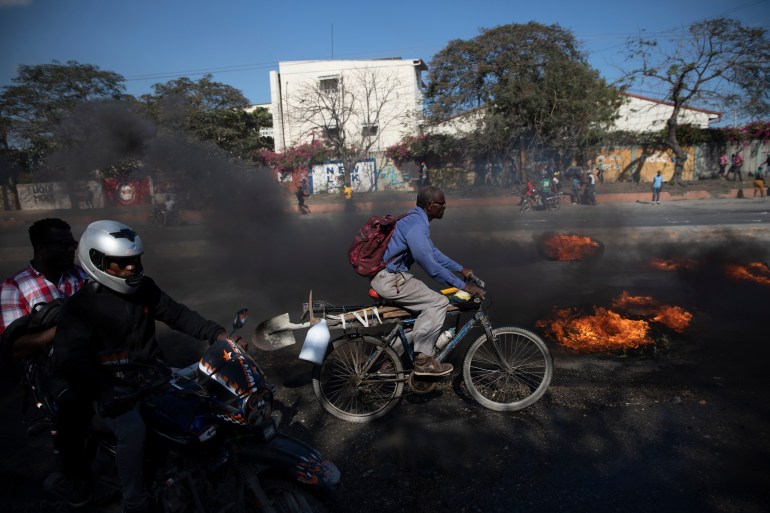 A bicyclist pedals past burning tires set on fire by factory workers demanding a salary increase, in Port-au-Prince