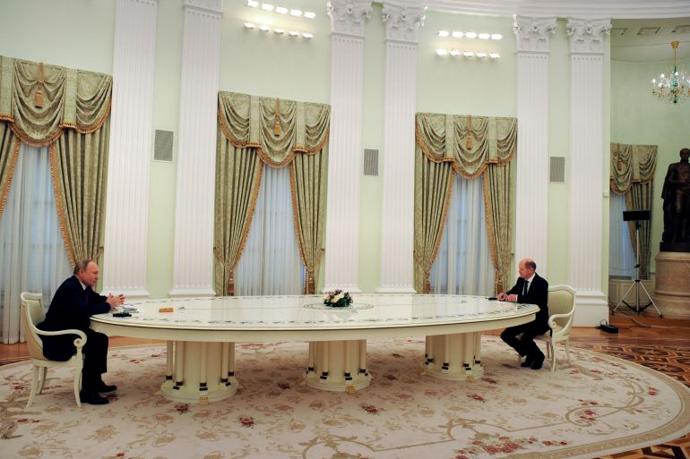 Russian President Vladimir Putin and German Chancellor Olaf Scholz sit at opposite ends of a very long table in a fancy room in Moscow