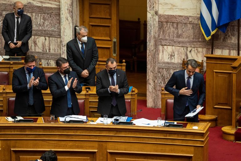 Greek Prime Minister Kyriakos Mitsotakis, right, is applauded by his party lawmakers