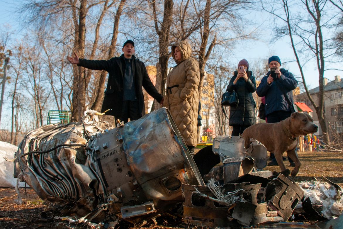 People stand next to fragments of military equipment on the street in the aftermath of an apparent Russian strike in Kharkiv