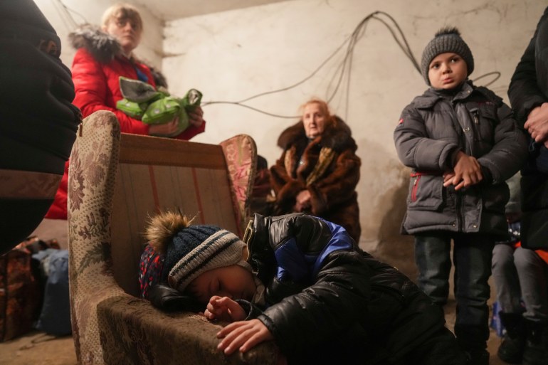 A child sleep in an armchair as other stand around in a shelter during Russian shelling, in Mariupol, Ukraine, Thursday, Feb. 24, 2022