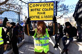 A demonstrator wearing a yellow vest holds a sign reading "Let's convoy our anger for our liberty"