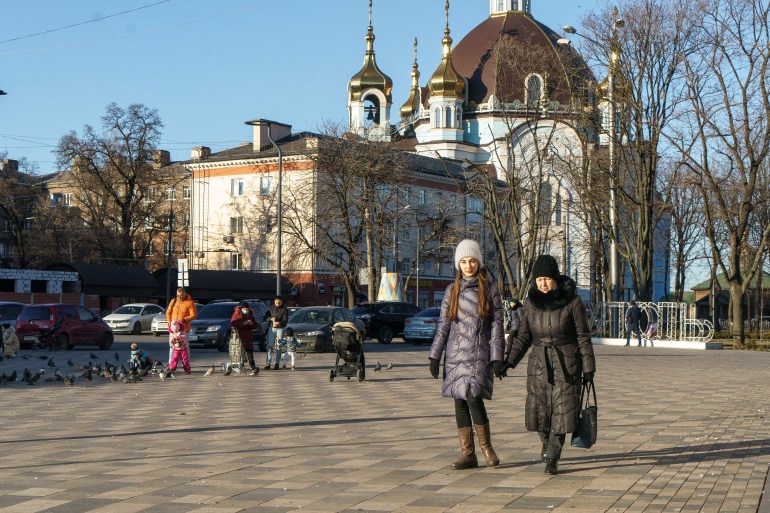 A young woman and an older woman walk along the street in Mariupol in the winter sun