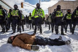 A protester lies on the snow in front of a line of police officers