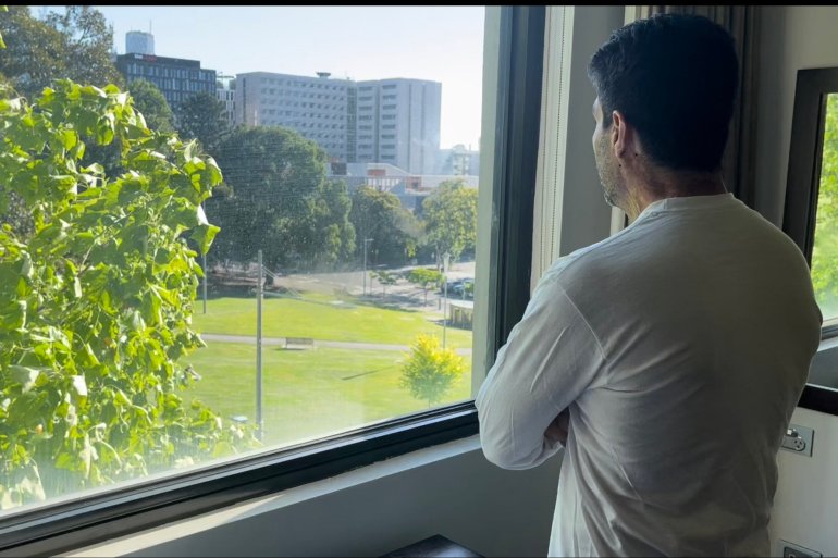 Jamal - in a white shirt with his face obscured - looks out of the window from his room in the Park Hotel to the green expanses of the park and its mature trees
