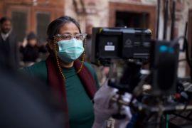 A photo of Meenu behind the camera with a mask and glasses directing a movie.