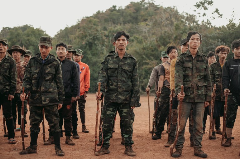 A group of trainee fighters holding wooden sticks to imitate rifles while they wait for more arms support.