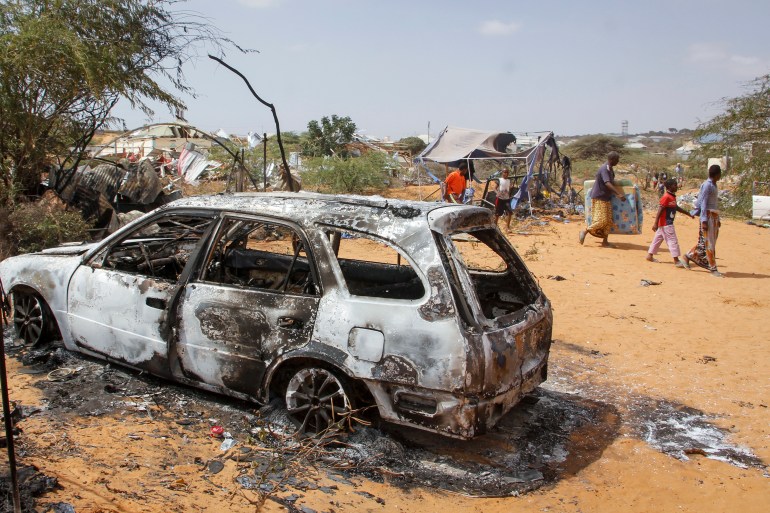 People walk past the wreckage of a vehicle destroyed in an attack outside of Mogadishu