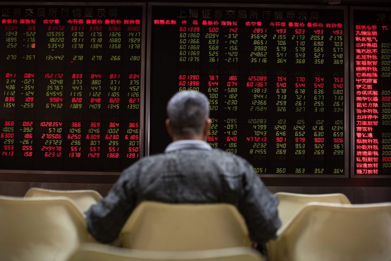 An investor looks at stock price movements on screens at a securities company in Beijing
