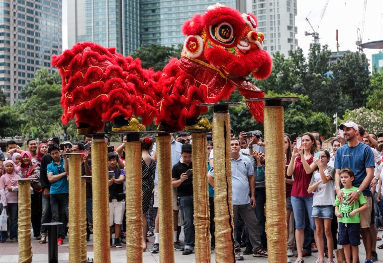 Lion dancer performers leap across tall poles in front of a crowd