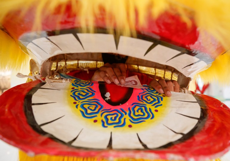 A close up of the lion's mouth with a yellow fringe and white teeth.  The dancer inside is counting tips that the audience stuff into the lion's mouth 