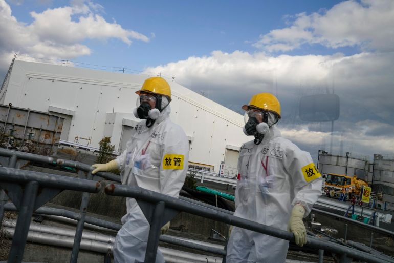 Workers wearing full protective suits and masks walk past the storage tanks for the wastewater at the Fukushima nuclear plant in Japan.