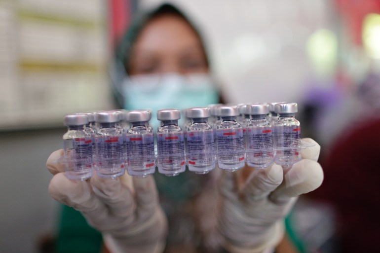 A masked female healthcare worker holds used vials of the Sinovac vaccine up the camera