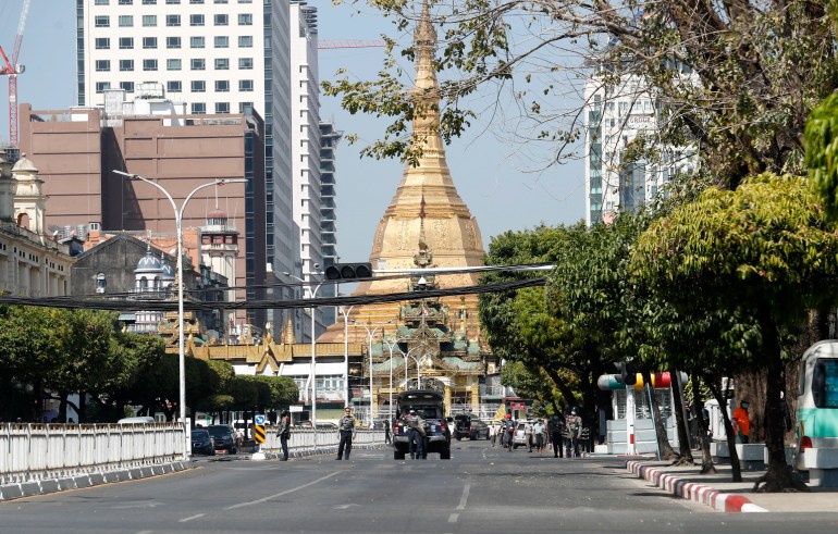 Soldiers man a barricade along a deserted street on front of the golden spire of Yangon's Sule Pagoda