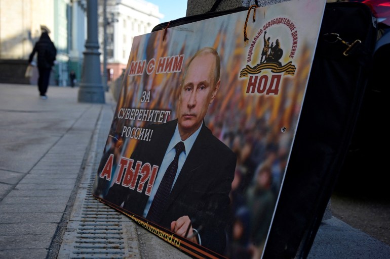 A placard featuring an image of Russian President Vladimir Putin and reading "We are with him for the sovereignty of Russia! And you?" is seen left in front of the Russian State Duma building in central Moscow on February 28, 2022. - The Russian army said on February 28, 2022 that Ukrainian civilians could "freely" leave the country's capital Kyiv and claimed its airforce dominated Ukraine's skies as its invasion entered a fifth day. (Photo by Natalia KOLESNIKOVA / AFP)