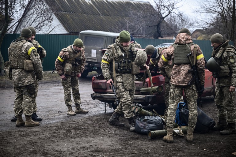 Ukrainian soldiers unload weapons from the trunk of an old car