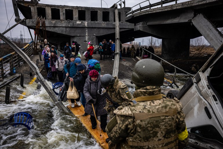 Evacuees cross a destroyed bridge as they flee the city of Irpin