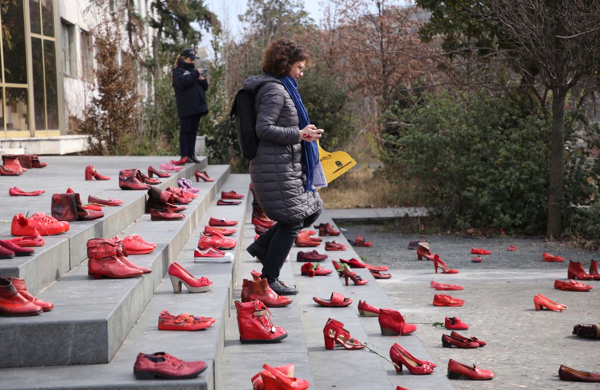 A woman walks past at an installation of women's red shoes displayed on a staircase, as a symbol to denounce violence against women, at Tirana's main square,
