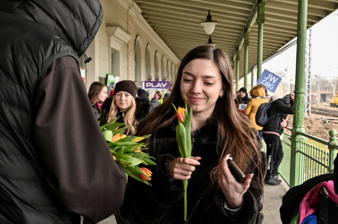 A woman smiles as she receives a flower from a Polish priest on the occassion of the International womens' day at the train station of Przemyl where hunderds refugees from Ukraine wait for their relocation, in Przemysl, Poland