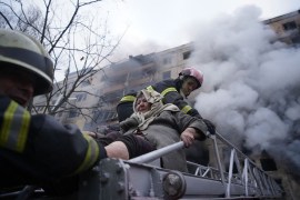 Firefighters help an elderly woman evacuate from an apartment hit by shelling in the Obolon district of Kyiv