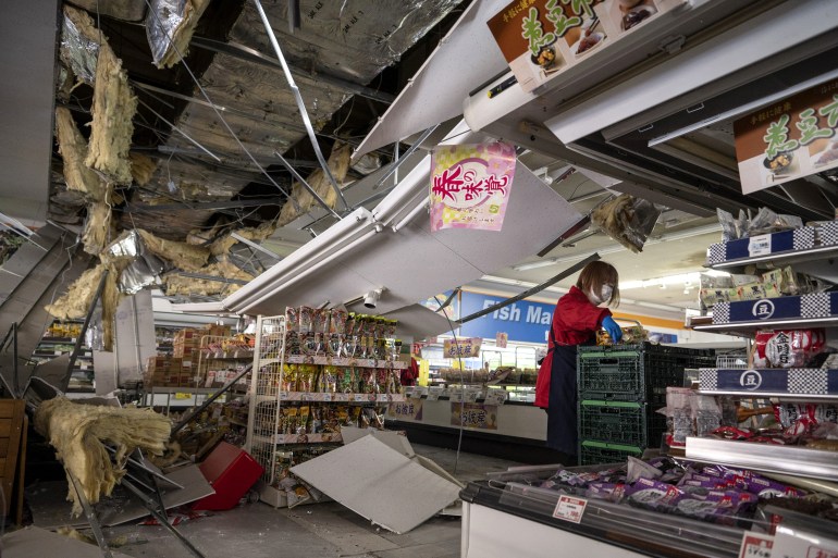 A woman in a supermarket cleans up after an earthquake in northeastern Japan with products thrown from shelves across the floor and the ceiling destroyed