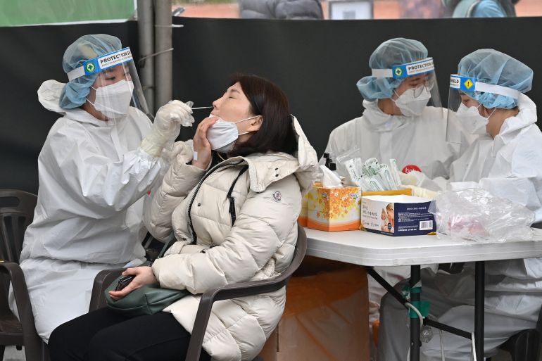 A woman in a thick winter coat is tested for COVID-19 by health workers in personal protective clothing at an outdoor testing centre in Seoul