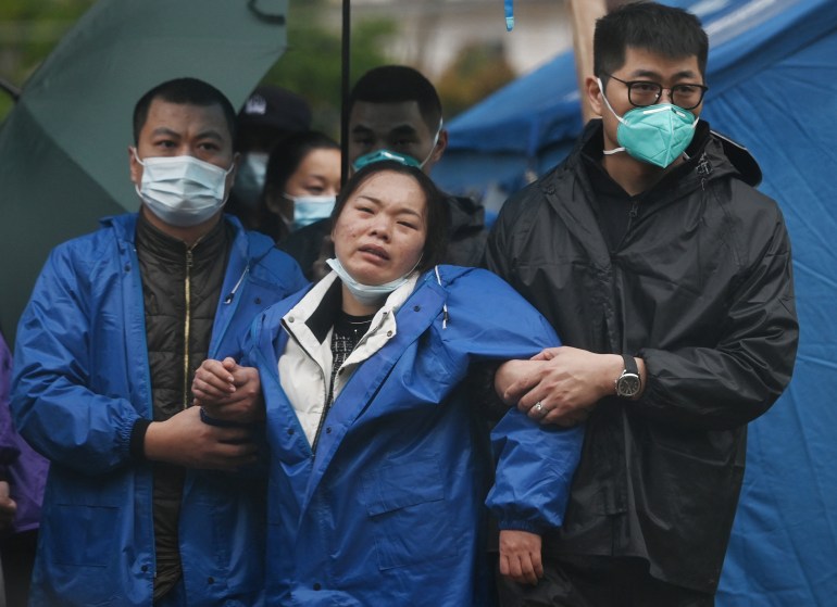 A grieving woman is held up by two men as she visits the site of the China Eastern crash