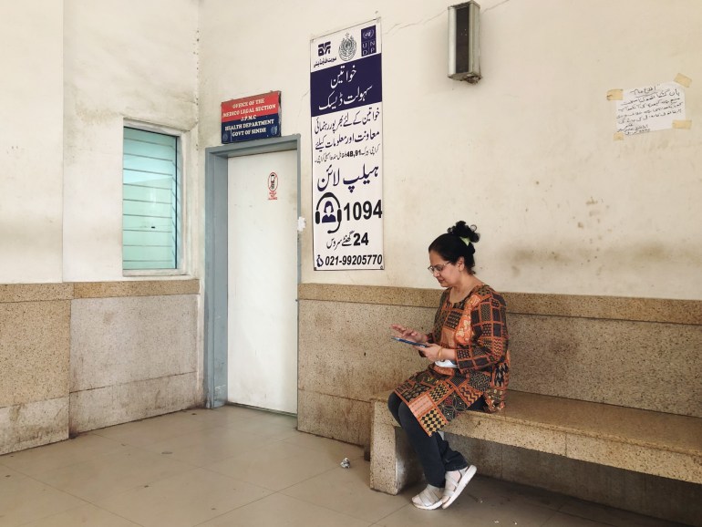 A photo of Dr Summaiya sitting outside the room where female patients/victims are taken to be examined, sitting on a bench and looking at her phone.