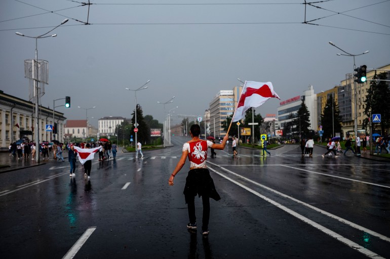 A photograph  of a pistillate   walking down   a thoroughfare  holding the Belarus emblem  successful  1  hand.