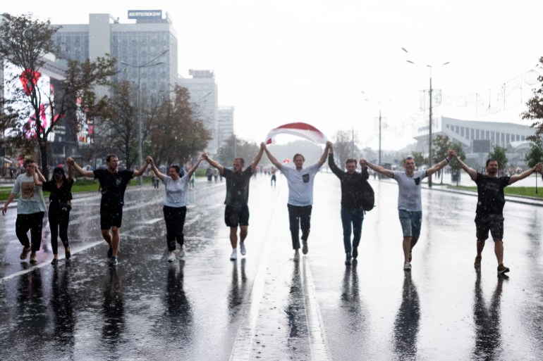 A photograph  of 9  radical   holding hands and walking successful  the mediate  of the thoroughfare  with a Belarusian flag.