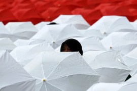 A woman peeks out from a sea of white and red umbrellas opened to create the Indonesian flag by members of NU