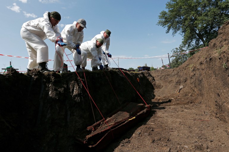 Volunteers lift a coffin from a mass grave in Donetsk