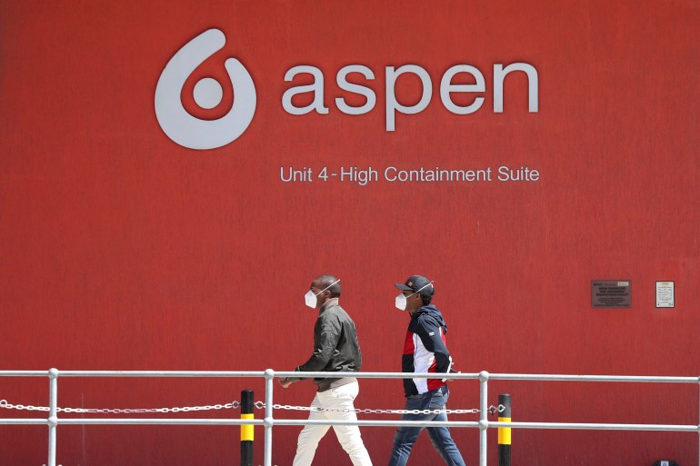 People wearing face masks walk past a logo of South African pharmaceutical major Aspen Pharmacare