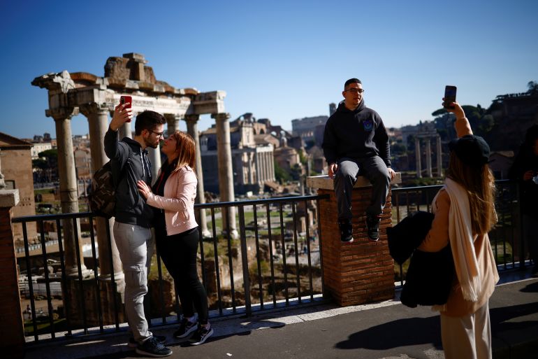 People pose for a photo without wearing face masks at the Capitoline Hill with the Roman Forum in the background on the day Italy's government lifted obligation to wear protective masks outdoor following a decline in COVID-19 cases, in Rome, Italy