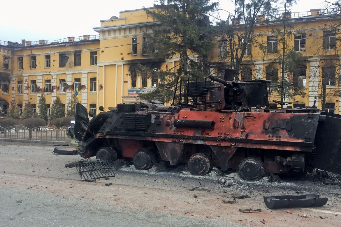 A destroyed Ukrainian armoured personnel carrier vehicle is seen in front of a school