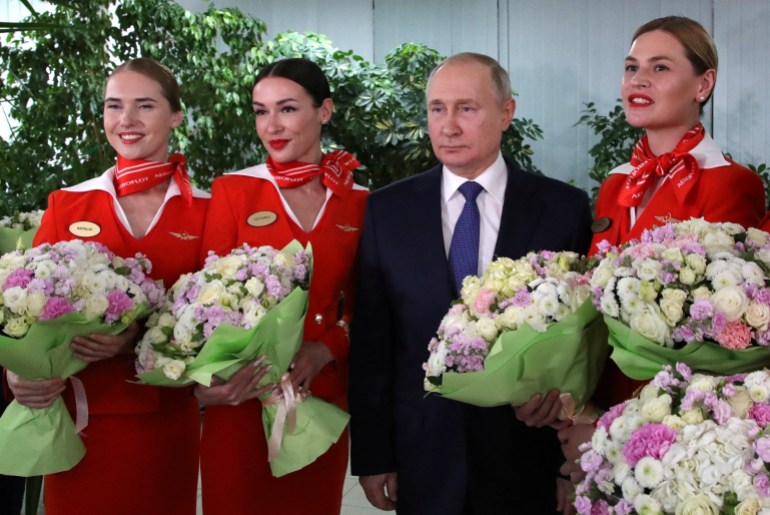 Putin stands next to Aeroflot stewardesses holding flowers