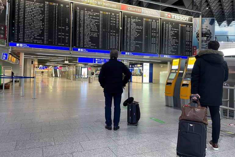 Passengers stand in front of a timetable showing many cancelled flights at Frankfurt Airport