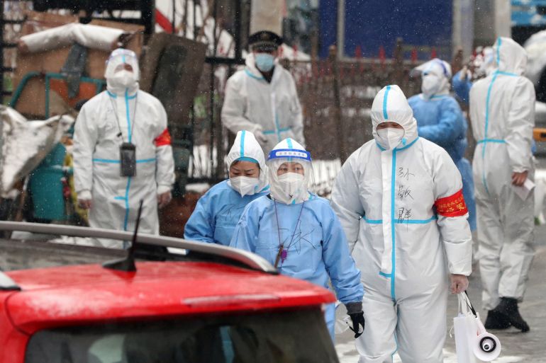 Medical workers in protective suits walk amid the snow as they enter a residential compound