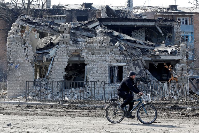 A local resident rides a bicycle past a destroyed building.