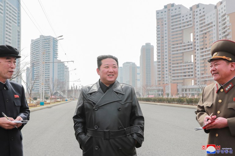 North Korean leader Kim Jong Un, wearing a black leather coat, stands in front of newly built housing blocks