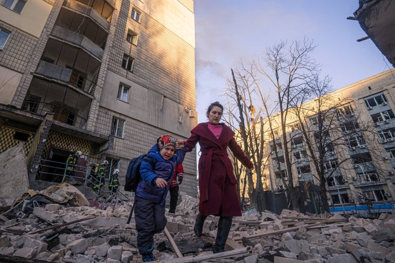 A woman with a child evacuates from a residential building damaged by shelling, as Russia's attack on Ukraine continues [State Emergency Service via Reuters]