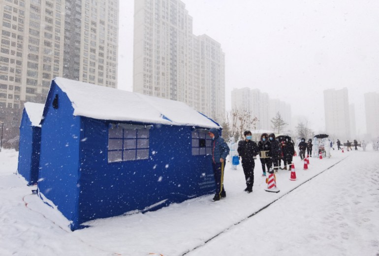 People queue in the snow outside a blue tent to get COVID-19 tests in Changchun in Jilin