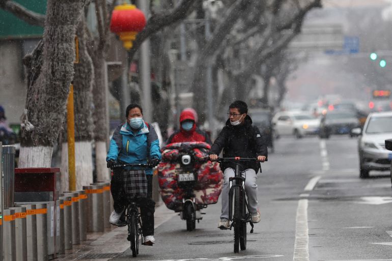 People ride bikes on a street amid snowfall, following the coronavirus disease (COVID-19) outbreak, in Beijing