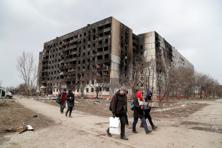 People walk along a street near a block of flats, which was destroyed during Ukraine-Russia conflict in the besieged port city of Mariupol,
