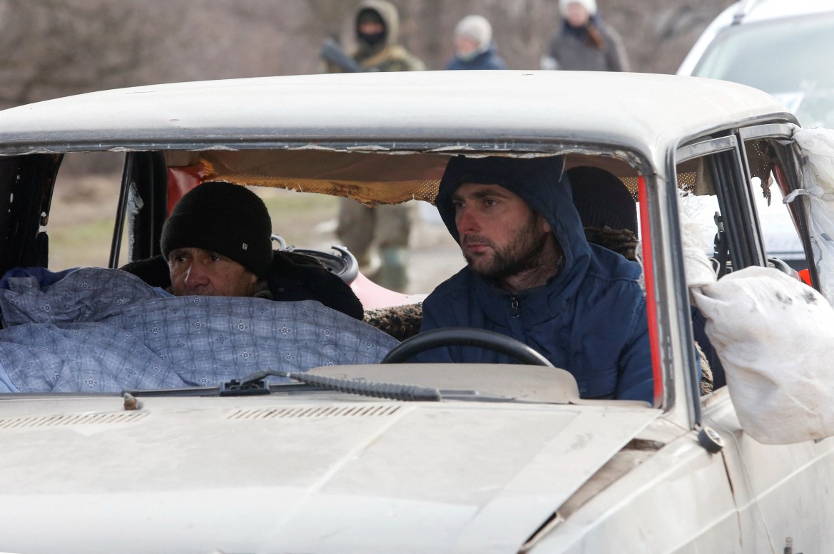 Evacuees fleeing Ukraine-Russia conflict sit in a damaged car as they wait in a line to leave the besieged southern port city of Mariupol