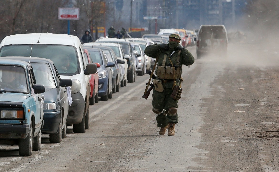 A service member of pro-Russian troops walks near a line of cars with evacuees, who leave the besieged southern port city of Mariupol,